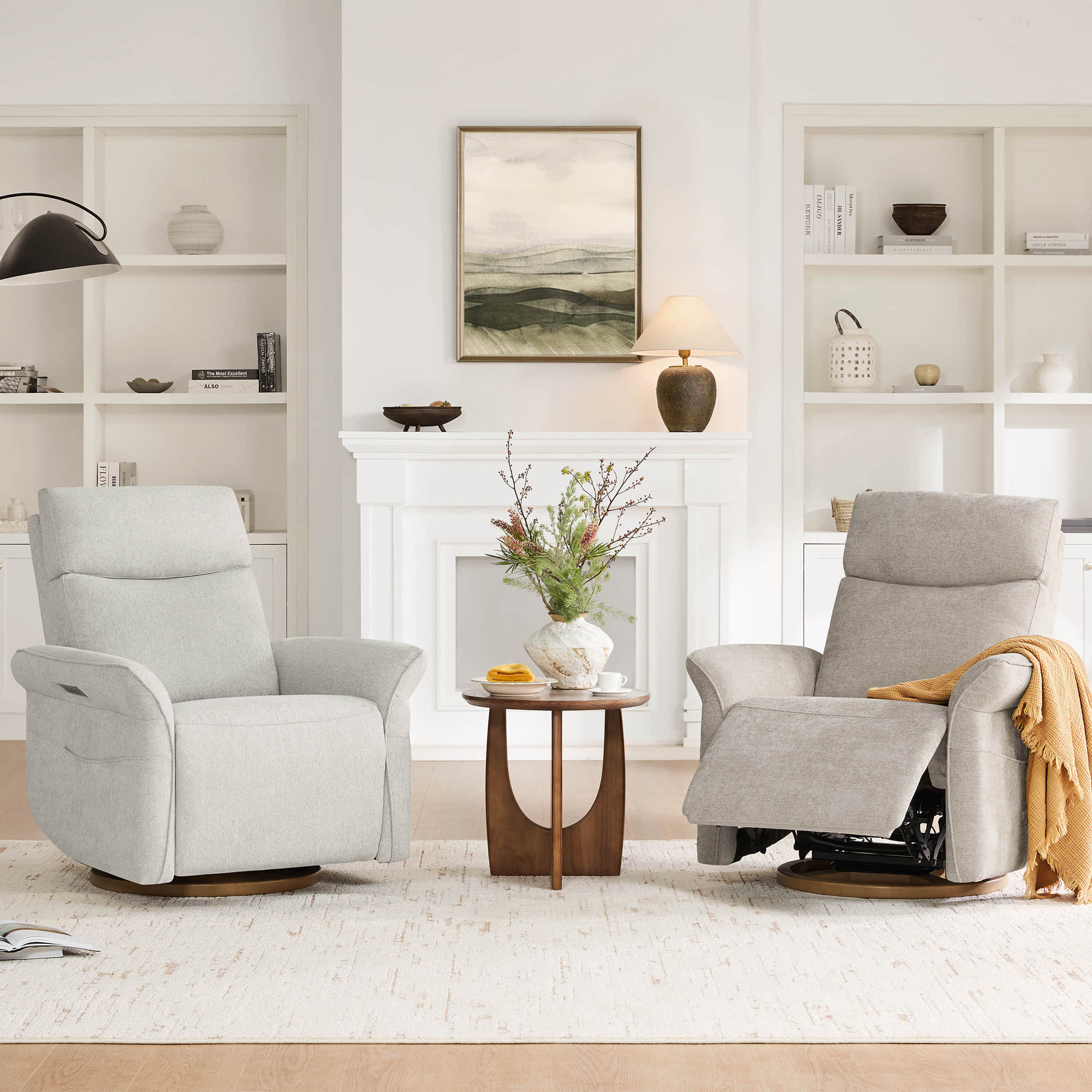 Two light grey swivel glider recliners in a cozy, bright living room setting.