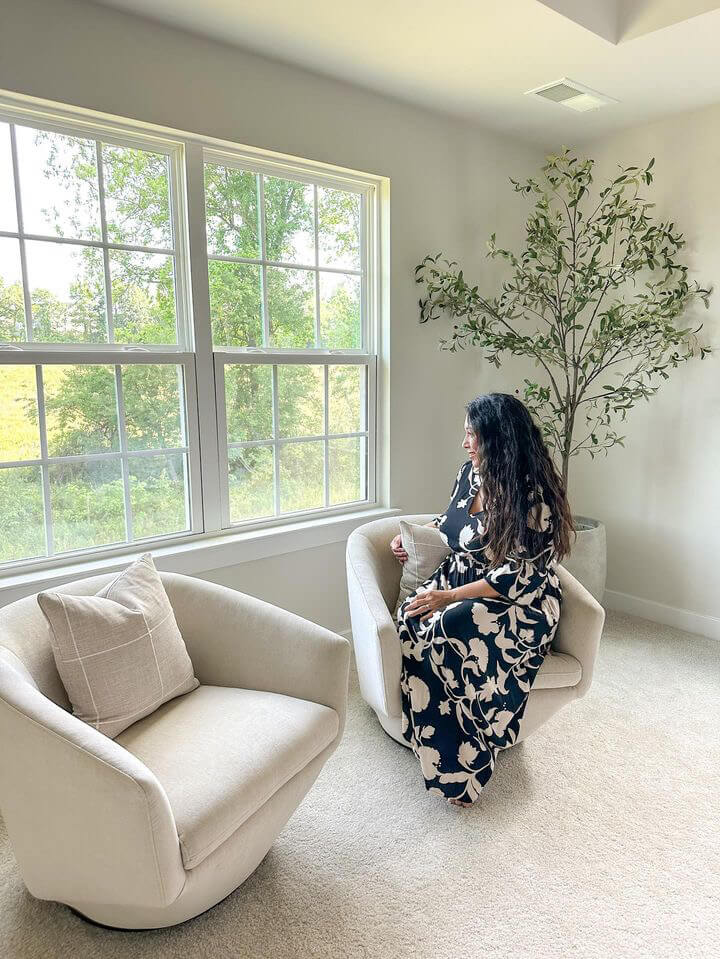 A woman in a black and white floral dress sits on a beige armchair