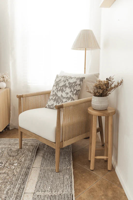 A cozy corner with a wooden armchair, a side table with a vase of dried flowers