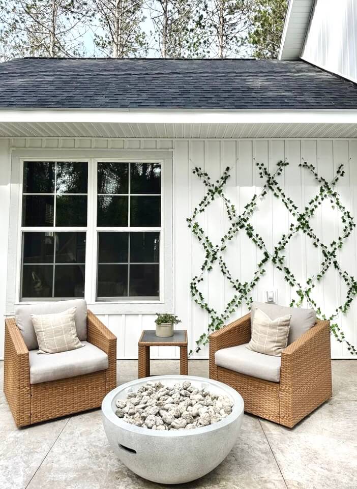 Two wicker chairs with cushions face a round fire pit filled with stones
