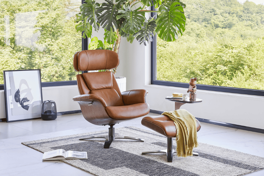 A brown leather armchair with a matching footstool in a bright room with large windows