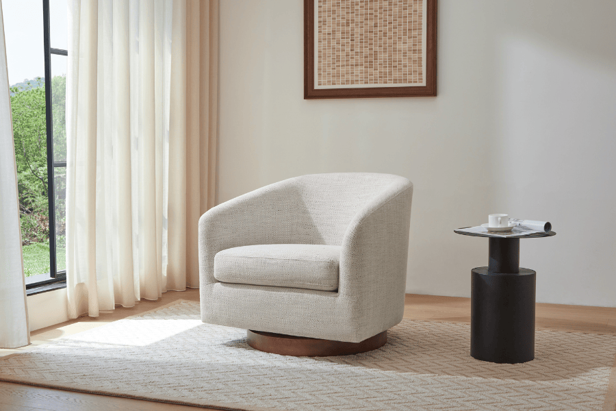 A beige armchair next to a small black side table with a cup and saucer, in a room with large windows.