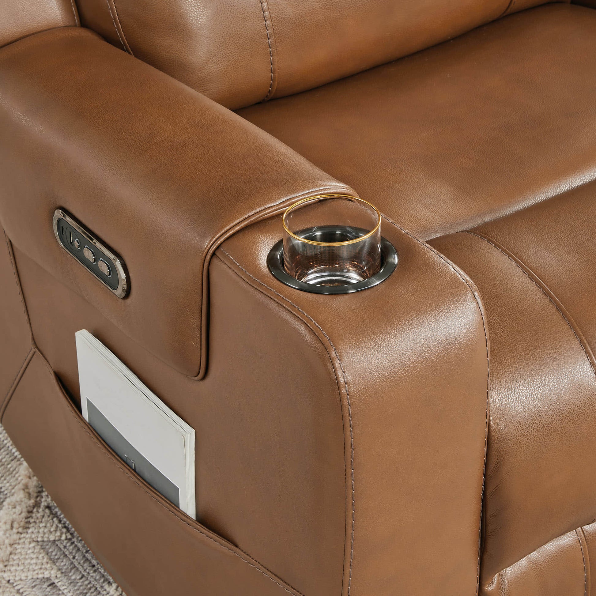 A tan leather recliner with a cup holder and a side pocket containing a book, in a cozy living room setting.