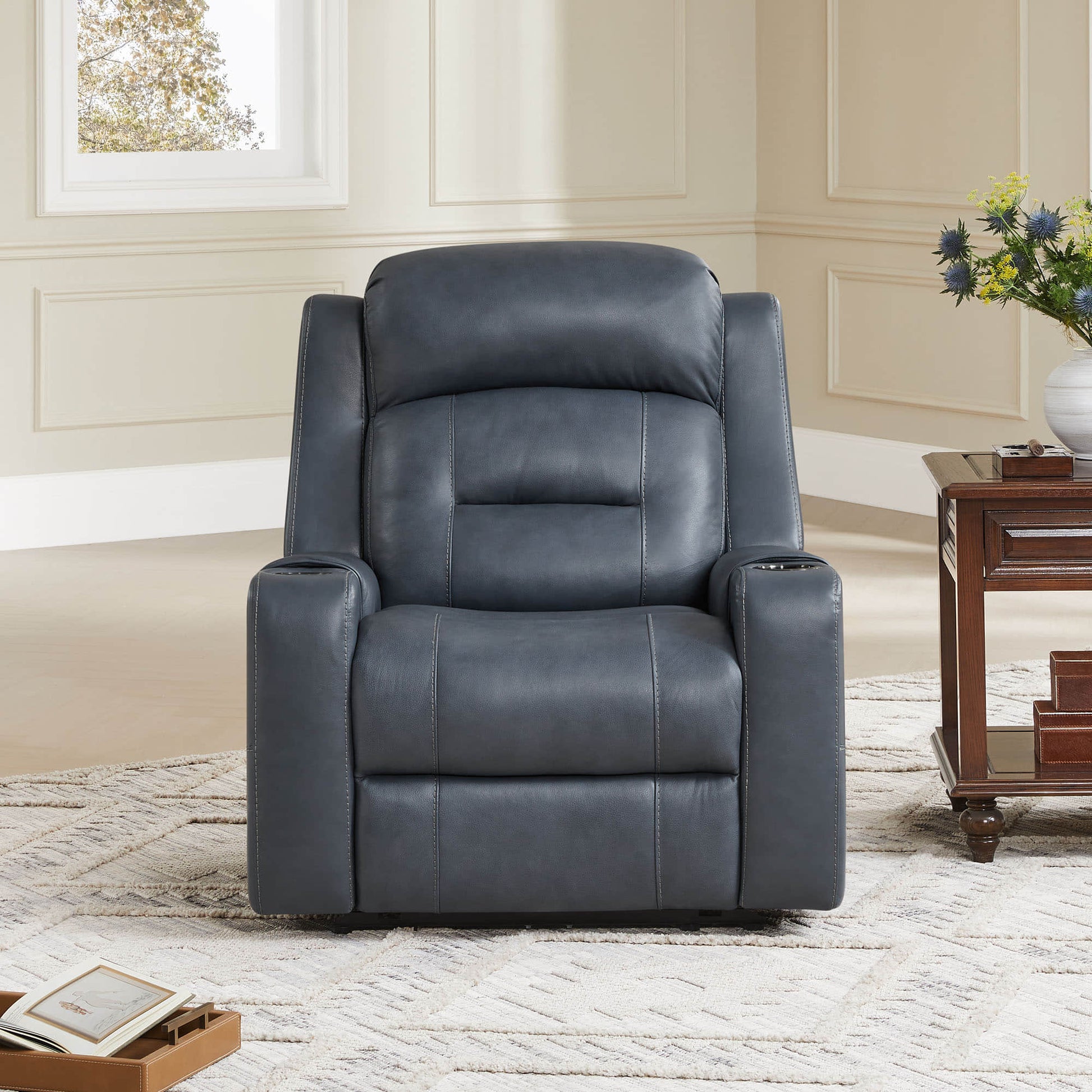 A dark blue leather recliner with cup holders, positioned next to a wooden side table in a cozy living room.