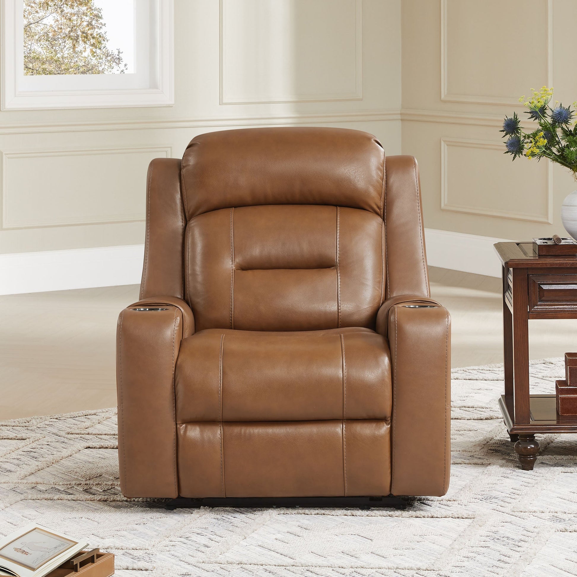 A tan leather recliner with cup holders, positioned next to a wooden side table in a cozy living room.
