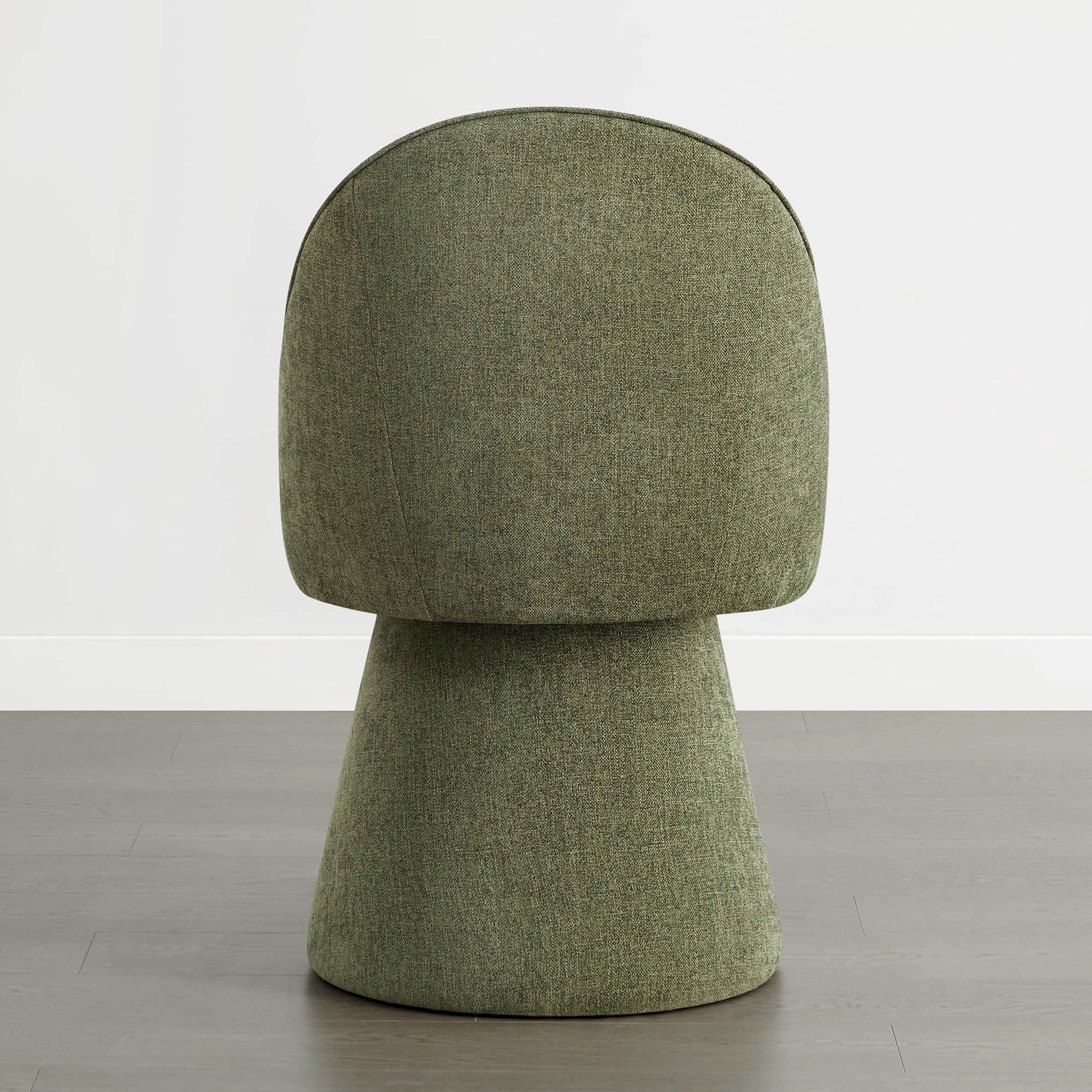 A green swivel chair viewed from the back, placed on a wooden floor against a white wall.