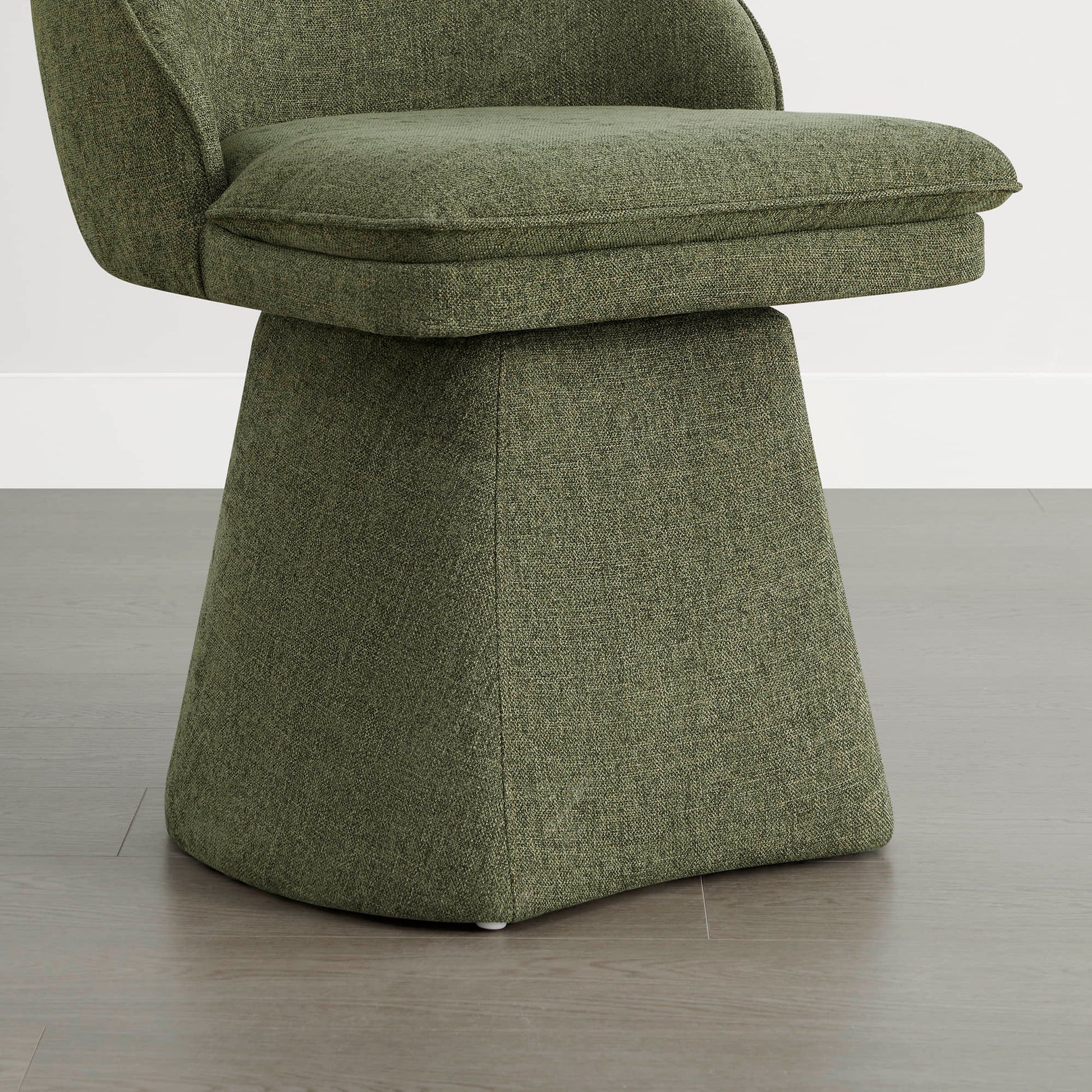 A close-up of a green swivel chair showing the cushioned seat and base, placed on a wooden floor against a white wall.