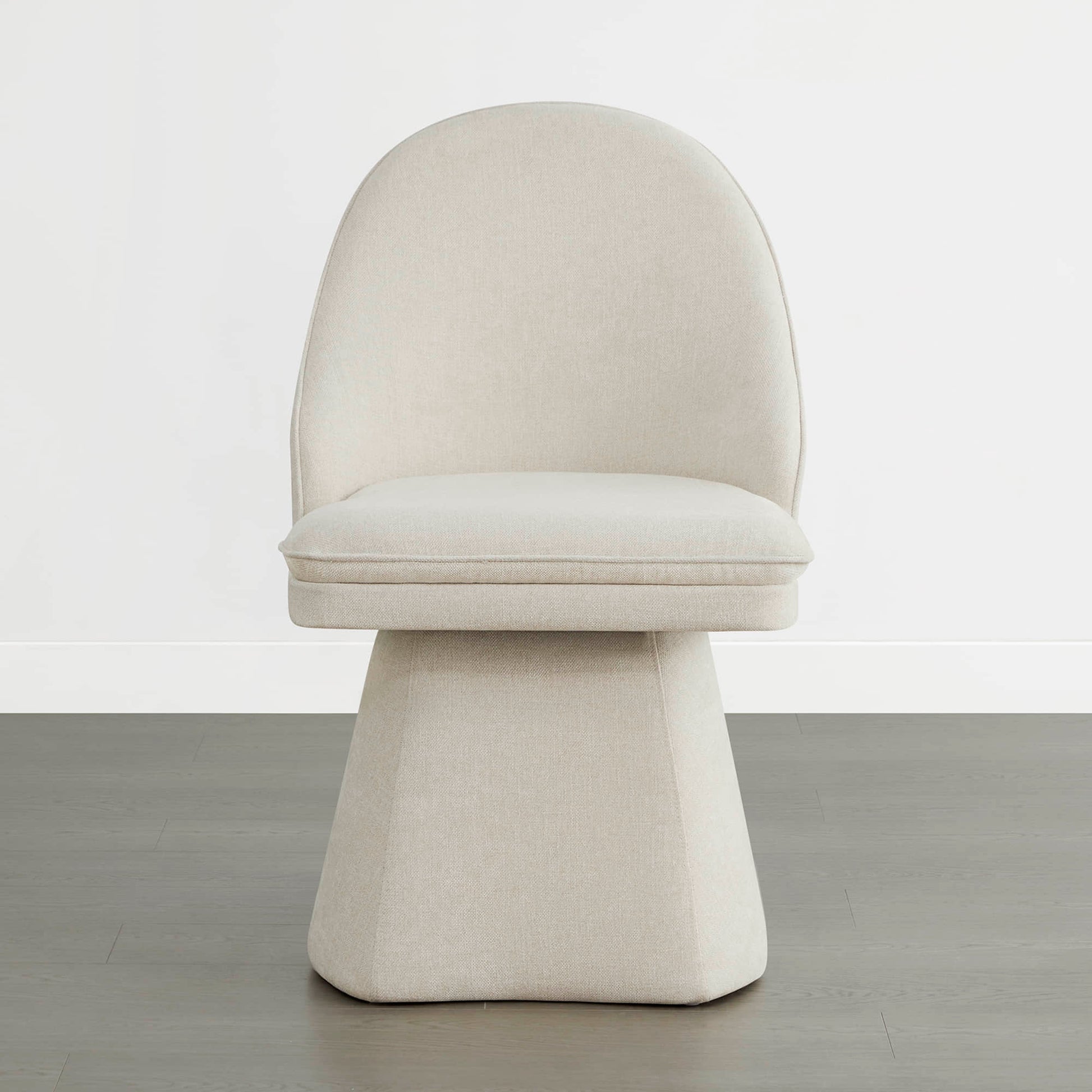 A single cream-colored swivel chair with a modern design, featuring a rounded backrest and a cushioned seat, placed on a wooden floor against a plain white wal