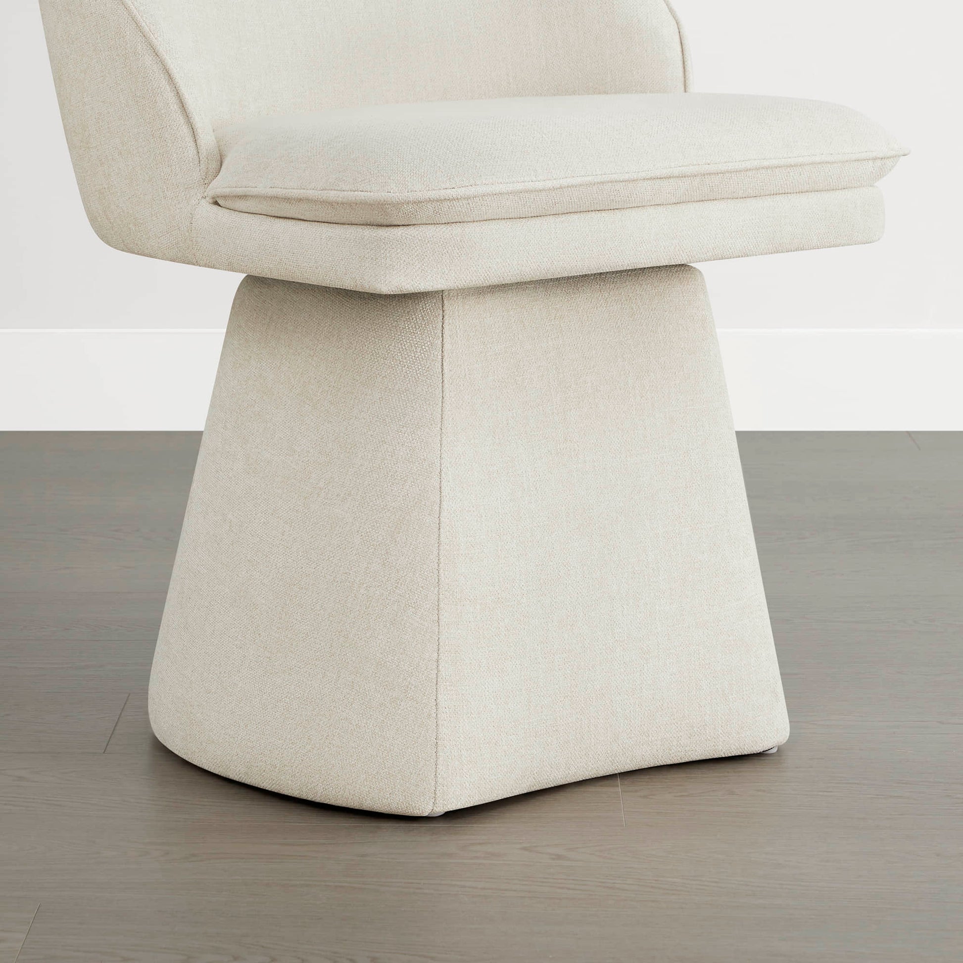 Close-up view of a cream swivel chair featuring a cushioned seat and a modern, tapered base design.