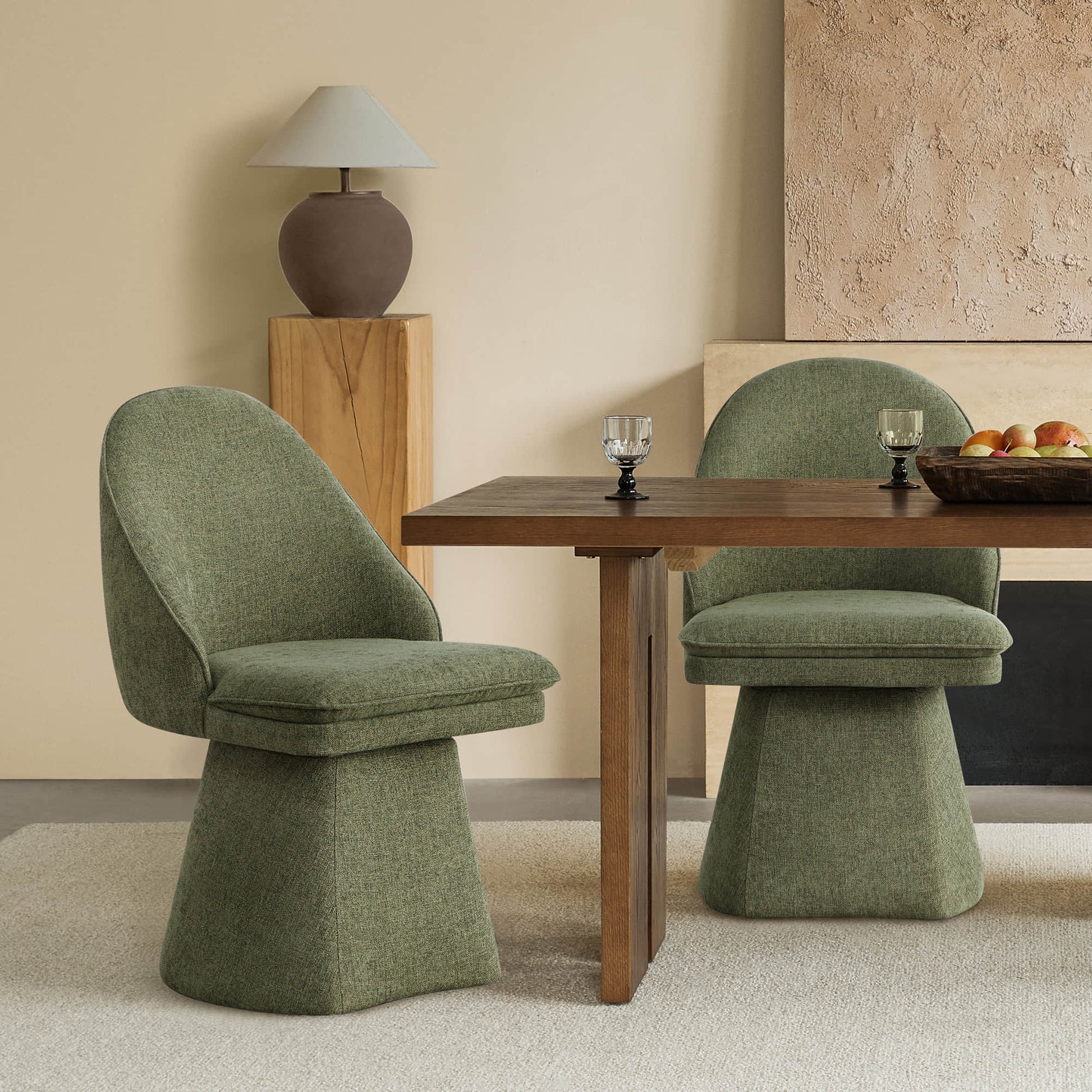 Two green swivel chairs at a wooden dining table, with a decorative lamp on a wooden pedestal and textured wall in the background.