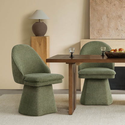 Two green swivel chairs at a wooden dining table, with a decorative lamp on a wooden pedestal and textured wall in the background.