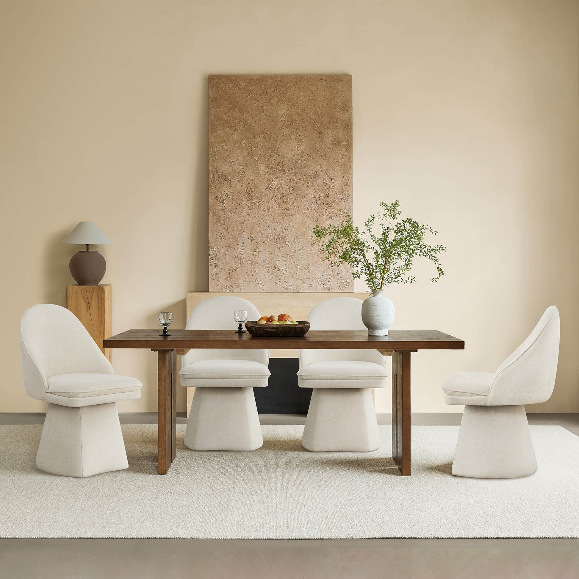  Four cream-colored swivel chairs around a wooden dining table, with a decorative vase and plant centerpiece, and a textured wall in the background.