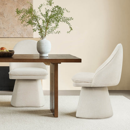 Two cream-colored swivel chairs at a wooden dining table, featuring a decorative vase with greenery, against a textured wall background.