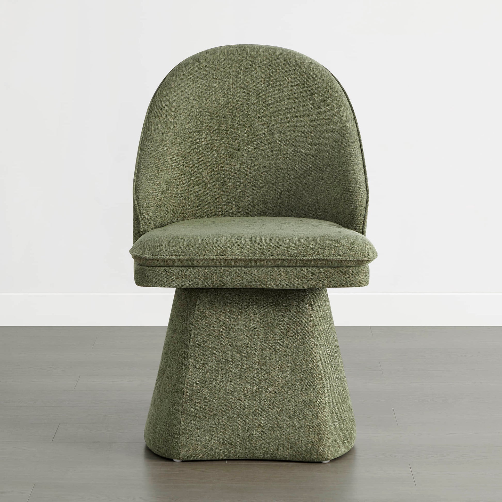 A single green swivel chair on a wooden floor against a white wall.