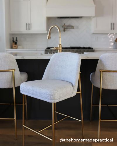 Three light gray upholstered bar stools with gold legs