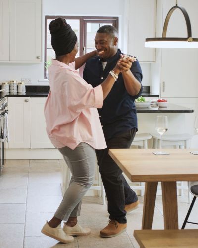 A couple dancing joyfully in a modern kitchen with white cabinets and a wooden table.