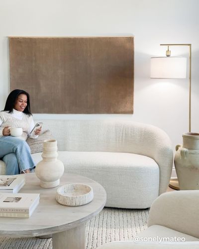 A woman sits on a modern sofa, holding a cup and a phone