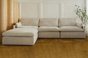 A beige sectional sofa with a chaise lounge in a room with wooden flooring and a plant.