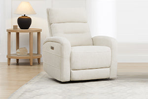 A white recliner chair next to a side table with a lamp in a bright room.