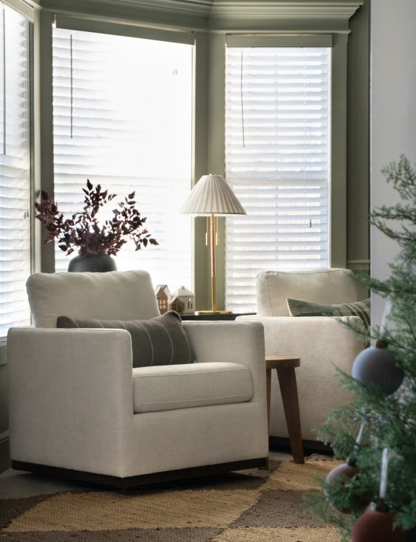 A cozy corner with two cream armchairs, a side table with a lamp and decor