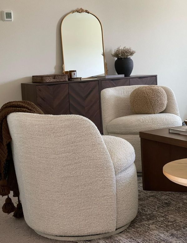 Two cream-colored armchairs with a round mirror and dark wooden cabinet