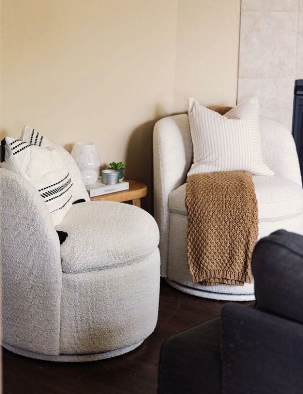 Two cozy, cream-colored swivel chairs with pillows and a throw blanket