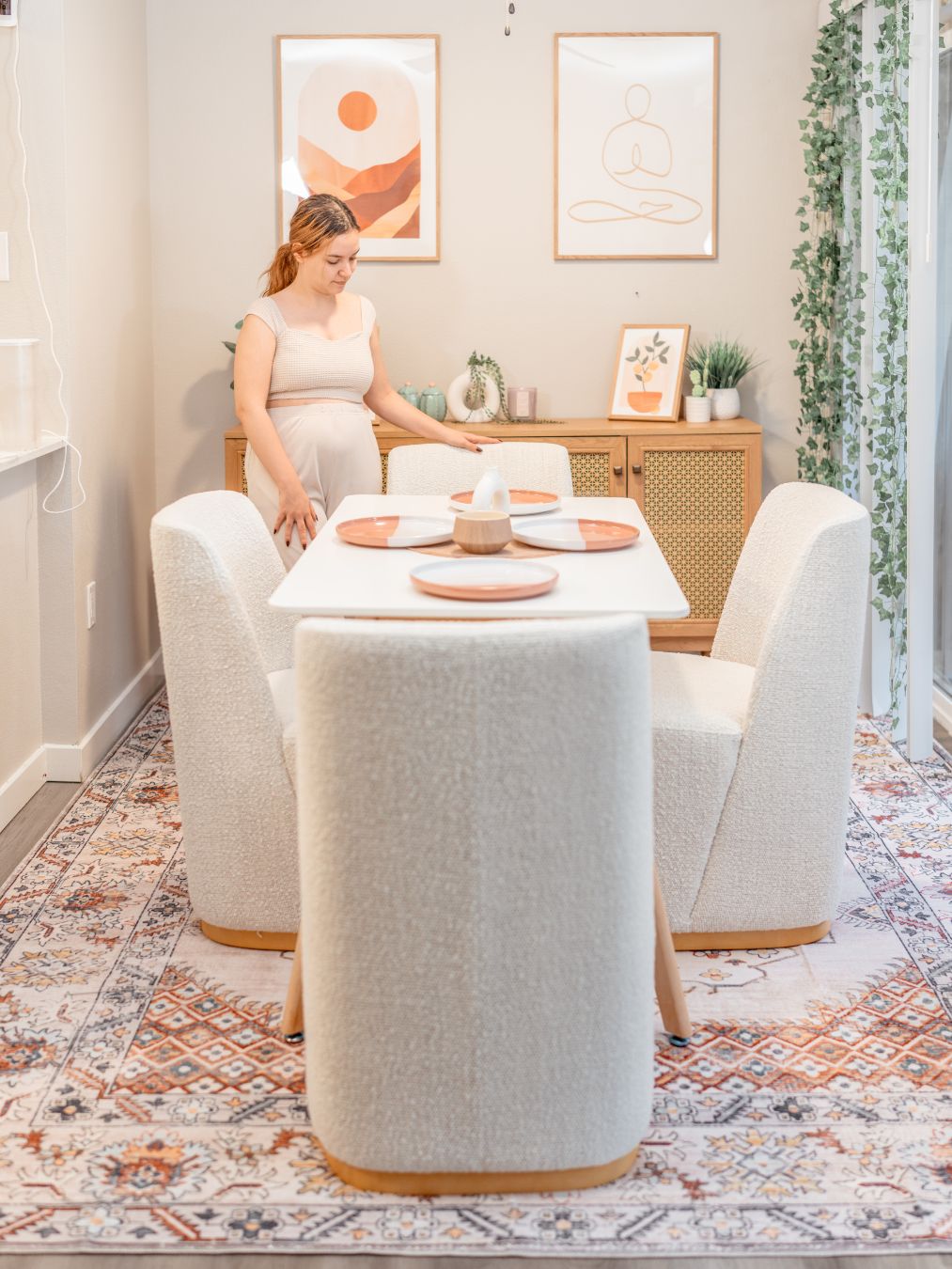 A woman sets a modern dining table with pink plates and white chairs
