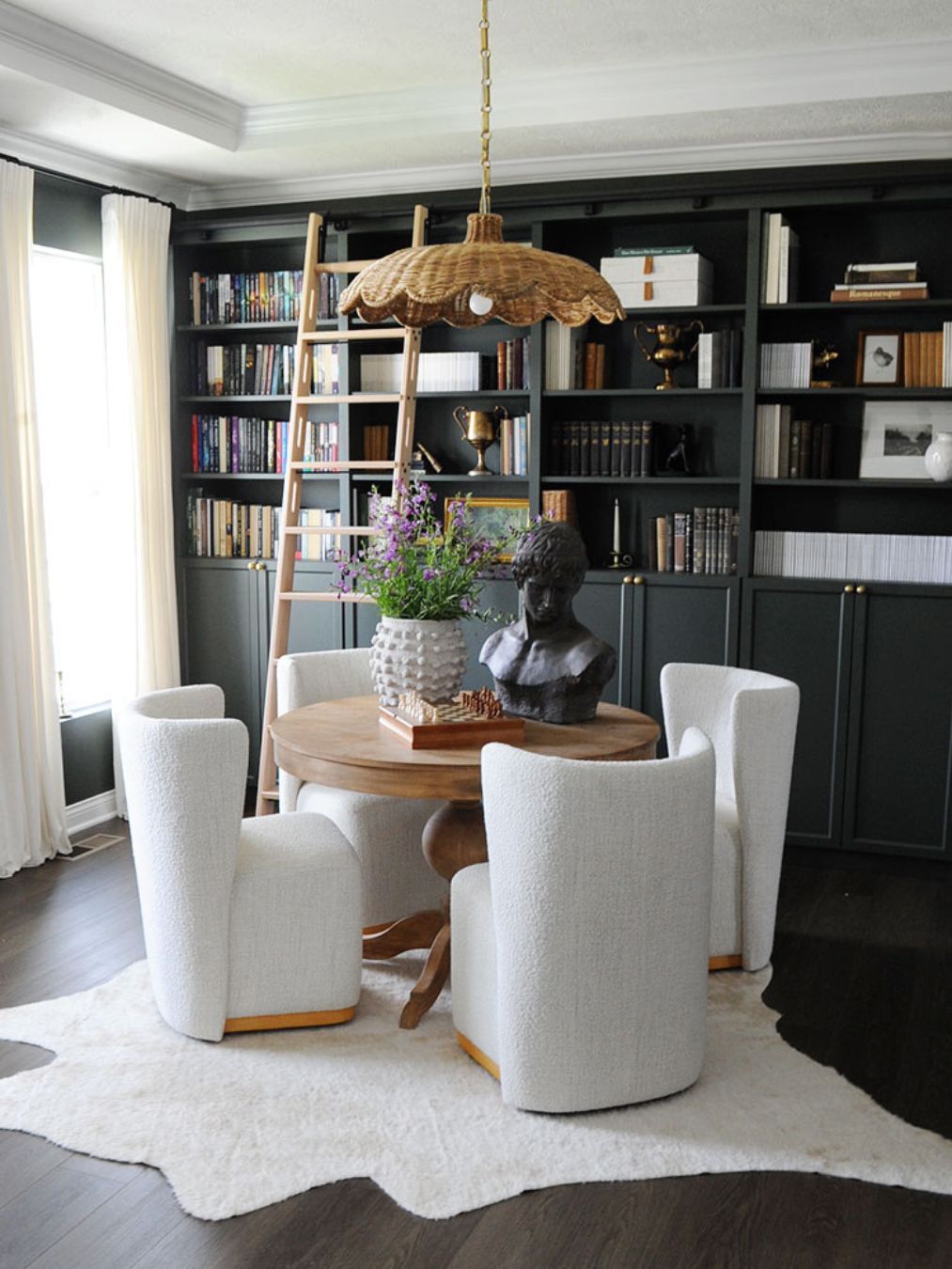 A cozy library with a round wooden table, white upholstered chairs