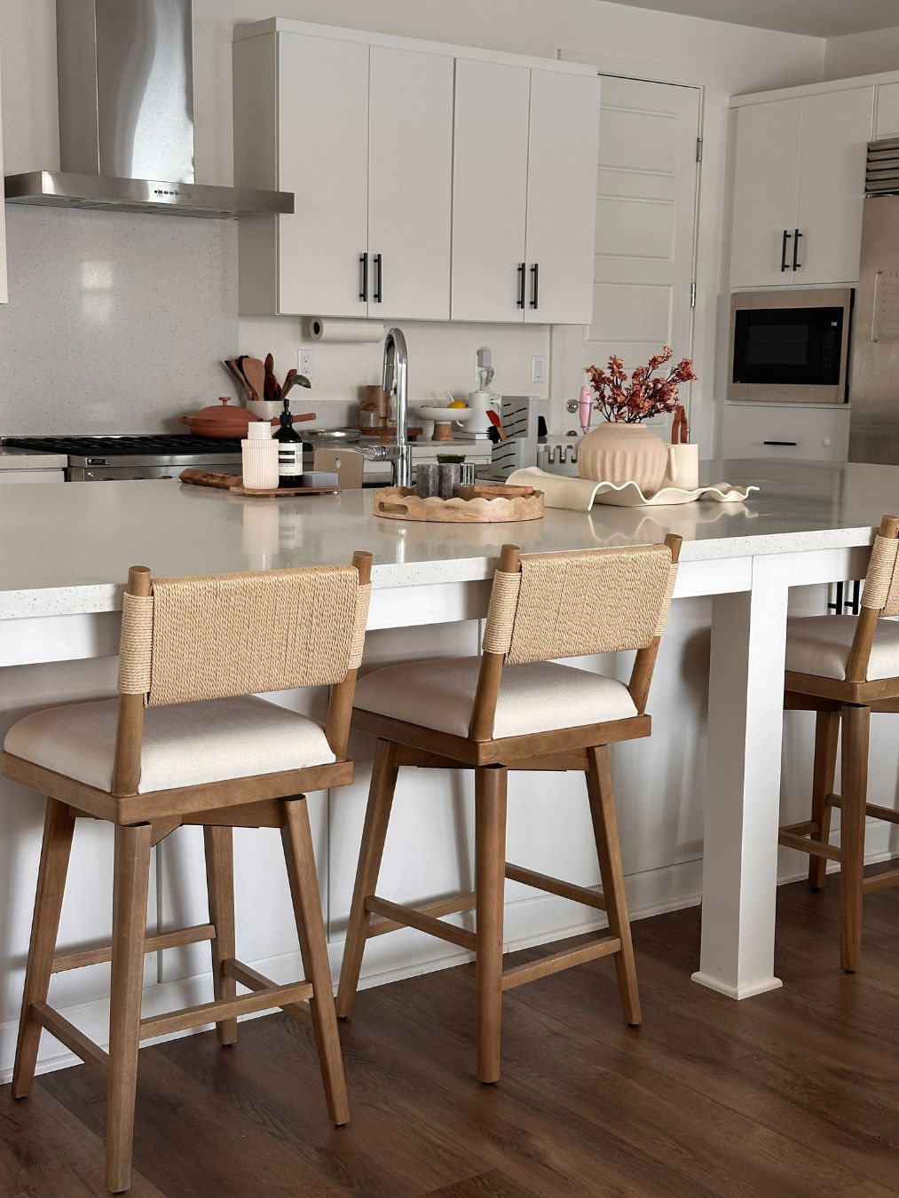 A modern kitchen with a white countertop, wooden bar stools with woven backs