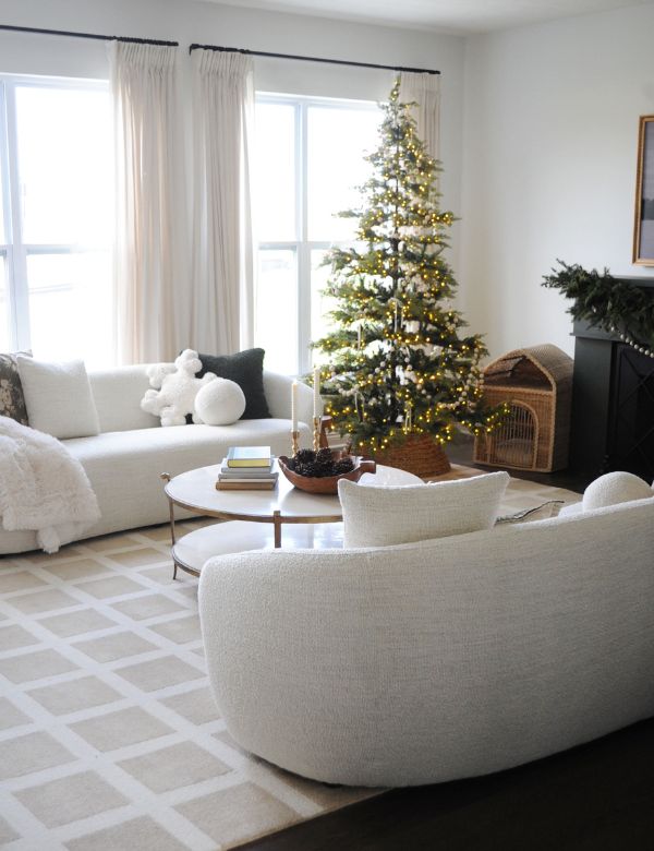 A cozy living room with a decorated Christmas tree, white sofas, and large windows.