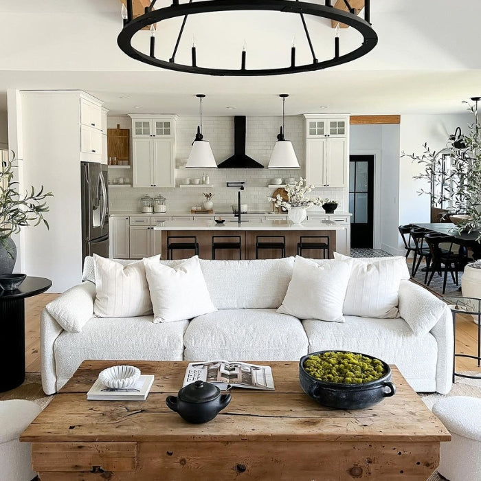 A white textured sofa with pillows, a rustic wooden coffee table holding a bowl of green fruit and decorative items.