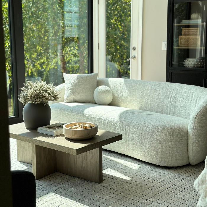 A textured white sofa with cushions, a wooden coffee table holding a book and a decorative bowl