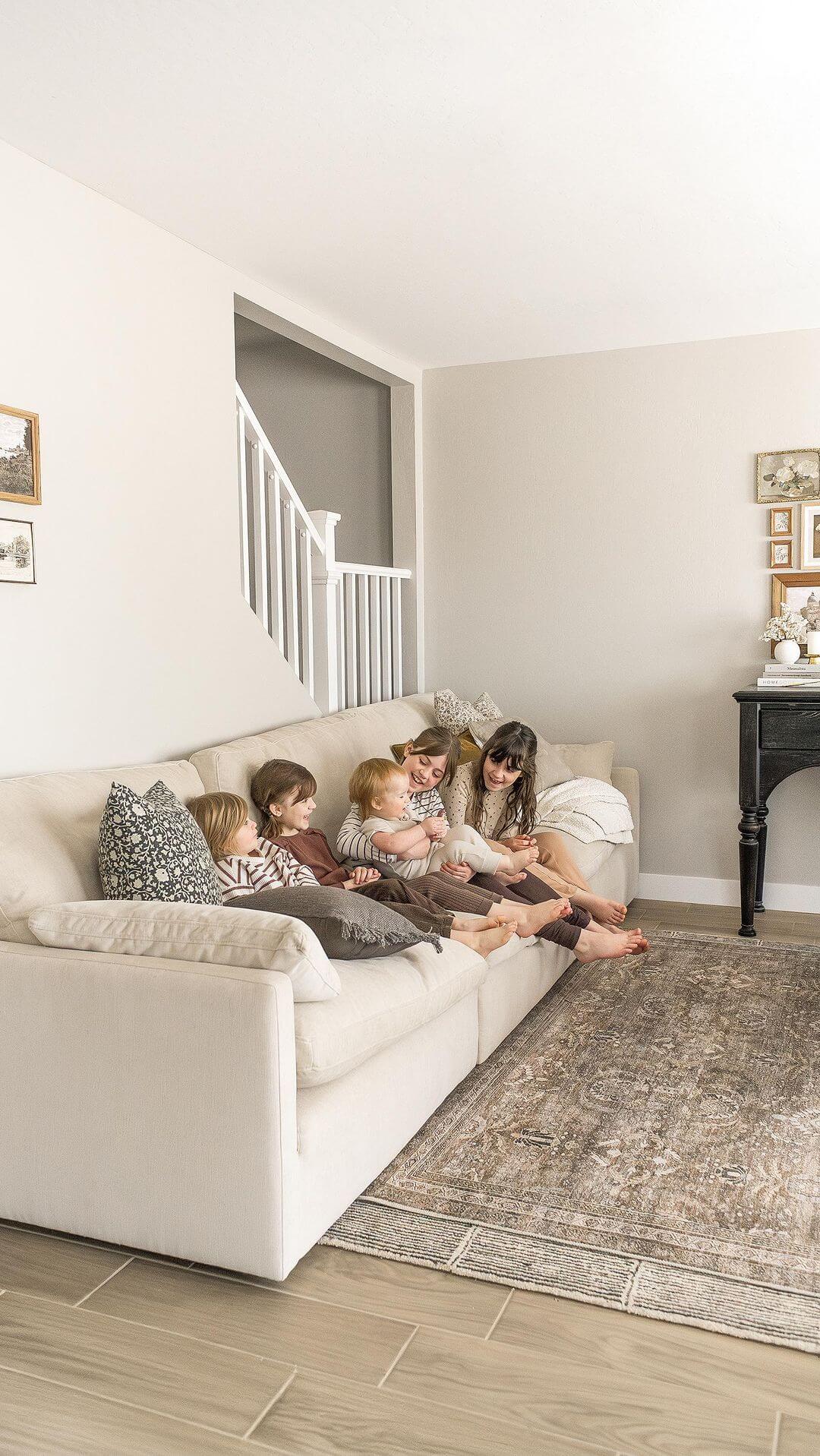 A family of five sits together on a beige sofa in a cozy living room